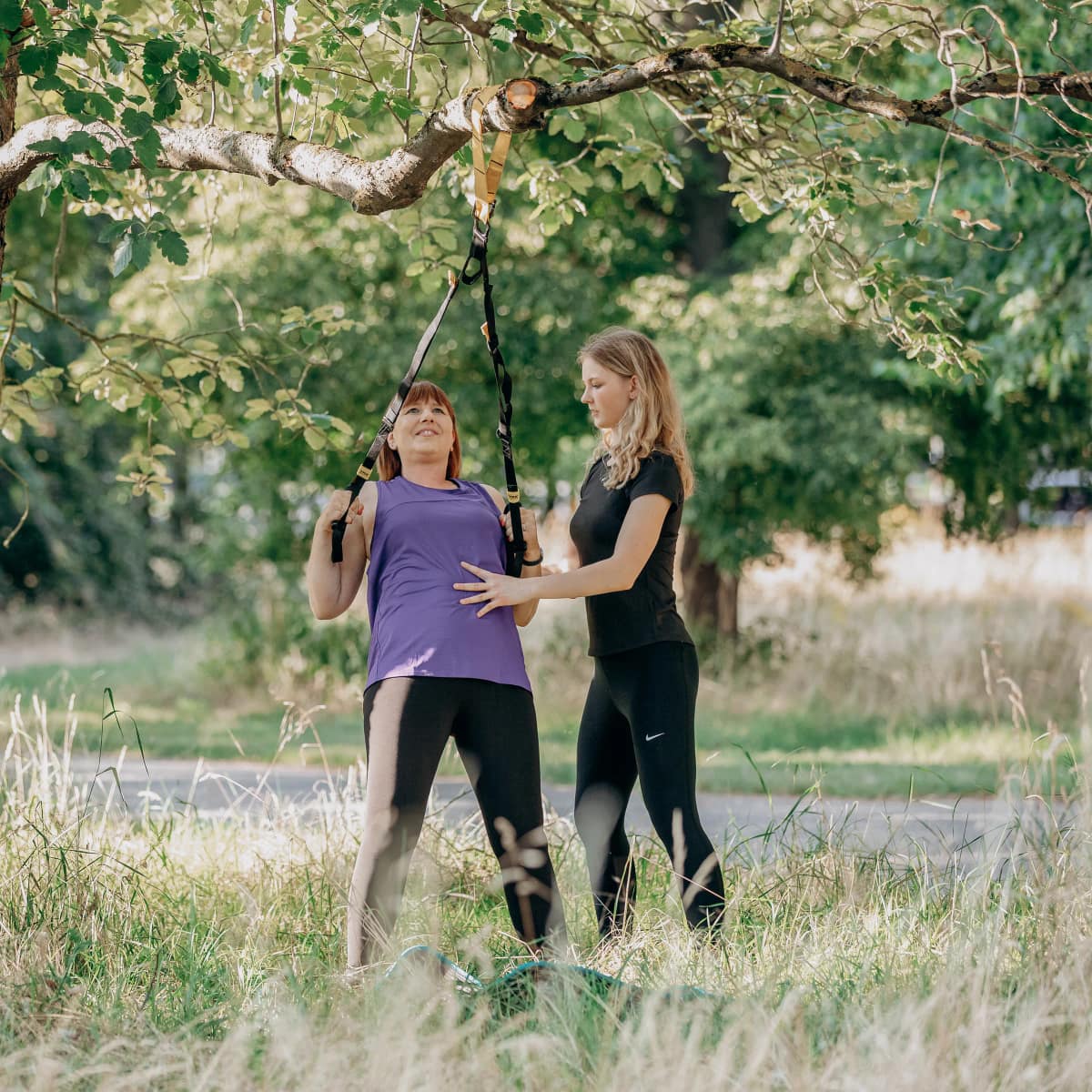 Personal Trainerin Lara Kölzow korrigiert die Haltung einer Kundin bei einer Übung mit dem Schlingentrainer, der an einem Baumast hängt